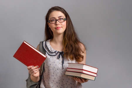 Education. A young woman or teenager wearing glasses, with a backpack on her back, holding a book in her hands. Copy space.の写真素材