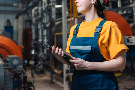 A female worker in uniform with a tablet in her hand. In the background boiler room. Concept of industrial production and equality. Close up.の写真素材