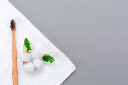 A white towel with a bamboo toothbrush and a cotton flower on it. Flat lay. Copy space. Gray background. Koncesja eco-friendly hygiene products.の写真素材