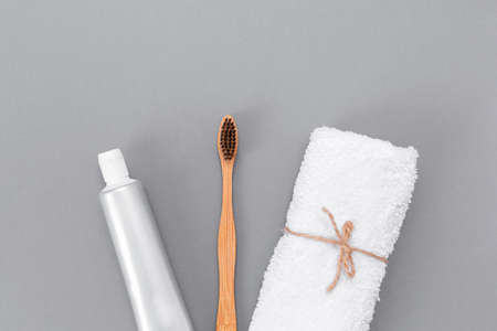 A roll of white towel, toothpaste, and a bamboo toothbrush. Flat lay. Gray background. The concept of eco-friendly personal care products.の写真素材