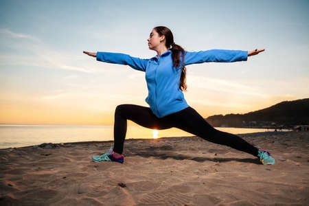 Young woman in sports clothes doing yoga on the beach. Sunset and ocean in the background. Wellness...