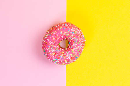 Round donut with pink icing. Pink and yellow background. Copy space. Flat lay.の写真素材