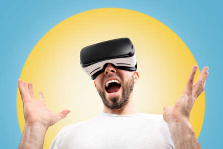 A wondered caucasian man in virtual reality glasses, with his mouth slightly open, spreads his...