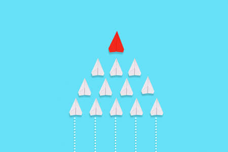 A red paper airplane leads a group of white airplanes. Blue background. Flat lay. The concept of...