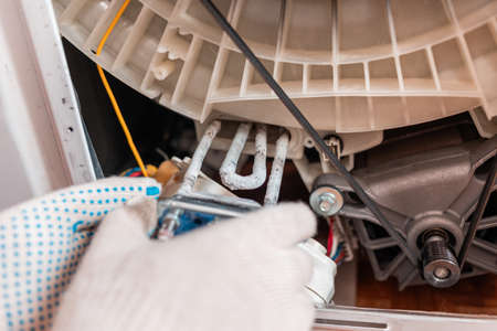 A worker takes out the broken heating element of the washing machine. Hands and spare part close-up....