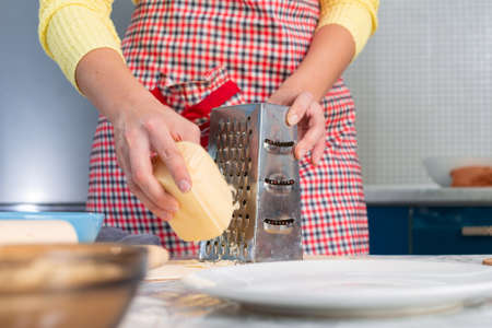 Woman in apron cooking in the kitchen, grating cheese. Hands close-up. The concept of a home-cooked...