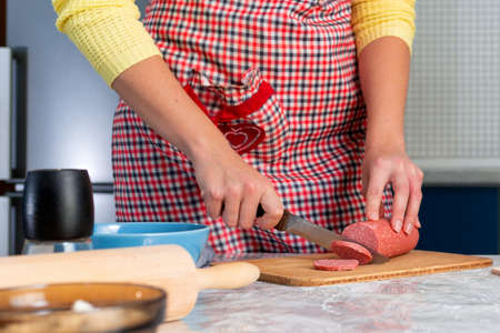 A woman in apron cooks in the kitchen, cuts sausage. Hands close-up. The concept of homemade food.
