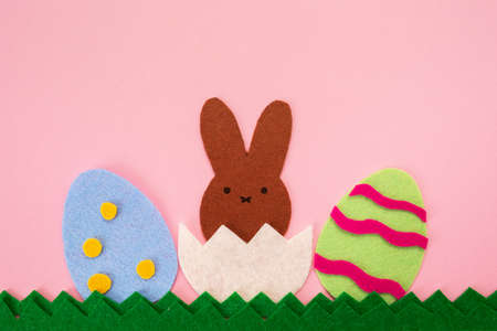 Easter decorations. Cut out the felt applications of two colorful eggs and brown rabbit hatched from the egg. Pink background. Flat lay. Copy space. Holiday concept.の写真素材