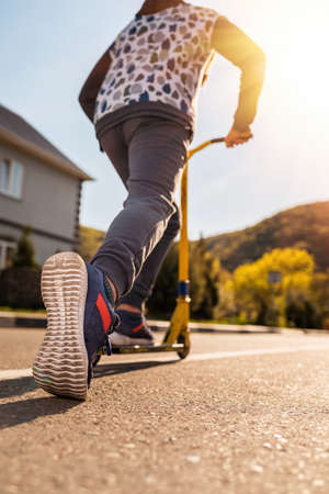 A teenage boy rides a scooter. Right foot in a sneaker close-up. Bottom and rear view. Empty street...