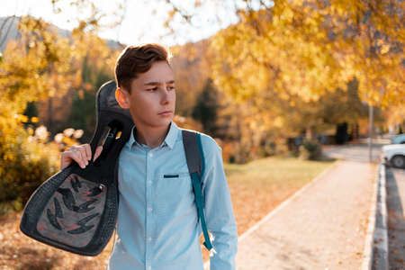 Teen boy holding a skateboard. In the background, a street with autumn trees.の写真素材