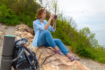 Young woman tourist is traveling through the mountains. A woman sitting on the rocks and takes a...