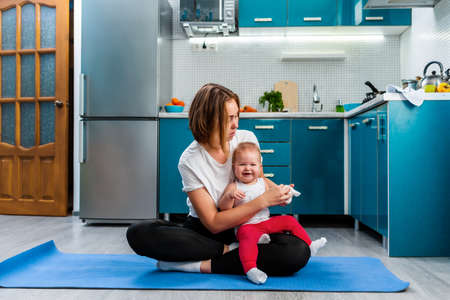 Sport and child education at home. A young mother sitting on a sports mat with happy baby and clothes a sock to him. The concept of yoga and baby's education.の写真素材