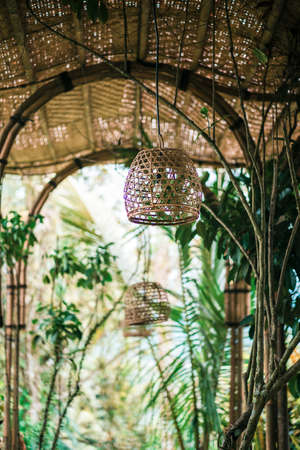 Tropical-style interior, wicker arches and lamps. In the background, tropical plants. Vertical.の写真素材