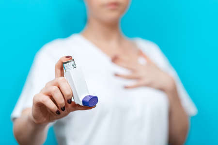 Symptoms of asthma. A woman in a blur shows an inhaler, and holds her hand to her chest. The background is blurred. In focus. Close up.の写真素材