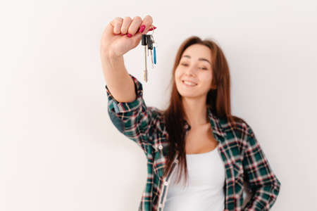 Buying and renting real estate. A smiling woman in a plaid shirt holds a bunch of keys. Hand with keys in focus, close-up. White background and copy space.の写真素材