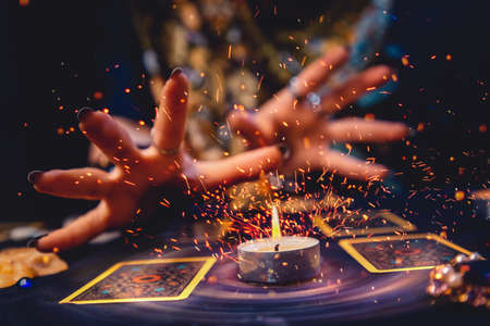 A witch's hands light the flame of a candle standing near two tarot cards. Close-up. Sorcery and astrology.の写真素材
