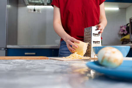 Woman cooking in the kitchen, grating cheese. Hands close-up. The concept of a home-cooked meal.の写真素材