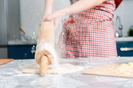 Housewife knocks the rolling pin on the table, over the dough lying on the kitchen table. Hands close up. Concept of homemade food.の写真素材