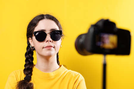 A young woman with glasses is streaming to the camera. Yellow background. The concept of vlogging.の写真素材