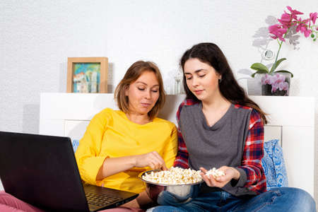 Two young Caucasian women watch a movie on a laptop and eat popcorn. The concept of relationships and LGBT.の写真素材