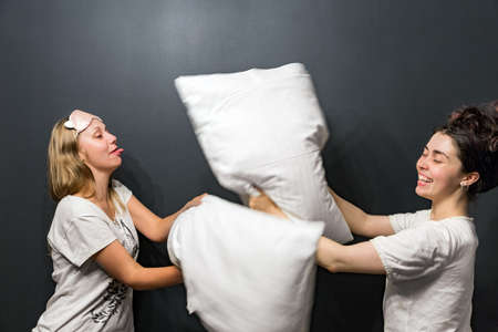 Girlfriends playing pillows on the black background.の写真素材