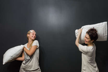 Two young womens fighting pillows on the black background.の写真素材