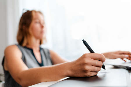 A blurry portrait of a young woman drawing on a tablet. Freelance and creative work.