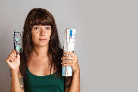 Young beautiful woman with glasses and a roll of magazine in her hands. Gray background. Copy space.