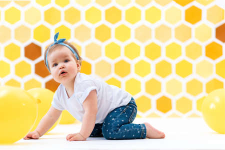 A female toddler crawling on a floor with yellow balloons. In the background is yellow honeycombs. World Children's Day.の写真素材