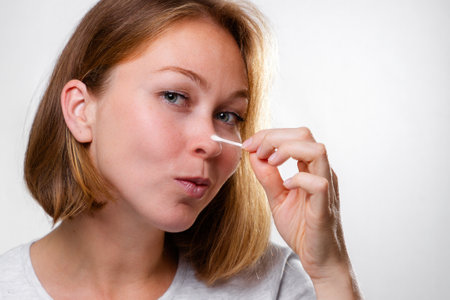 Portrait of a young woman smearing medicine on a pimple on her nose. White background. Acne and pimples concept.の写真素材