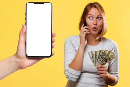 A rurprised girl holds a fan of dollars and talks on the phone. On the left is a smartphone with a...