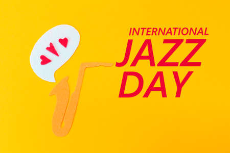 A cutted out of felt saxophone from which hearts flew out, on a yellow background. Flat lay. International Jazz Day.の写真素材