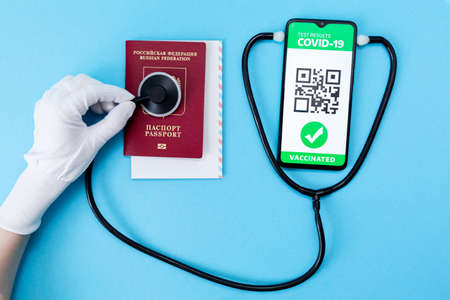 A hand in protective glove control aa passport with help of a stethoscope. Cellphone screen with an electronic health passport with qr-code. Flat lay. Concept of Covid-19 test for travel.の写真素材