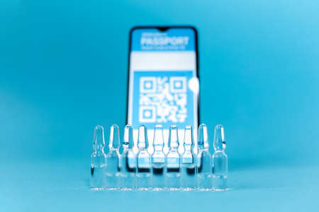 Close up view ampules with vaccines and blurred smartphone with electronic Immunity passport. Blue...