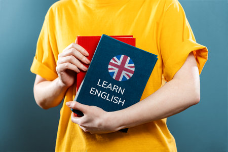English Language Day. A woman holds English textbooks in her hands. Close-up of books. Blue background. The concept of learning foreign languages.の写真素材
