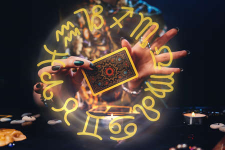 Witches hands holding a Tarot card. The zodiac circle surrounds the hand. Concept of astrology and esotericism.の写真素材