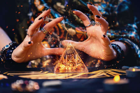 A witch conjures a magic glass pyramid. Hands close-up. Sparks flare up near the pyramid. The concept of witchcraft and divination.の写真素材