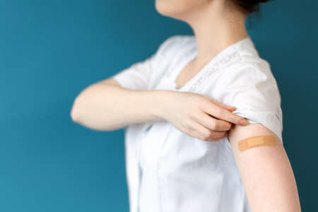 Nurse shows a hand with a bandaid stuck on it. Close-up. Dark blue background. Concept of immunization and virus protection.の写真素材