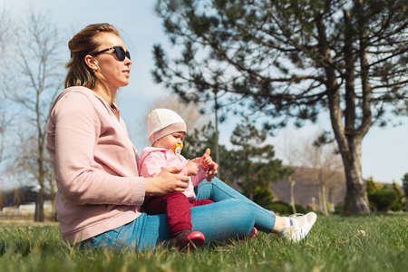 A mother sits on the grass, hugging her baby. Walking and outdoor recreation with children.の写真素材