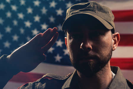 Memorial day. A portrait of uniformed soldier salutes against the background of the American flag. Close up. The concept of the American national holidays and patriotismの写真素材