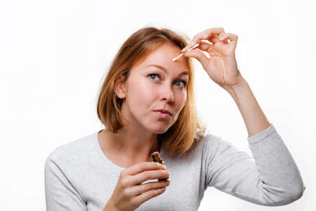 Portrait of a young woman smearing medicine on a pimple on her forehead. White background. Acne and pimples.の写真素材