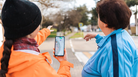 A young woman holds a smartphone with an online map and shows the way to an elderly woman with her hand. Mature woman was lost in the city. Concept of memory loss and dementia.の写真素材