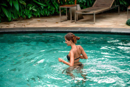 Tanned beautiful woman comes into the pool. Copy space.