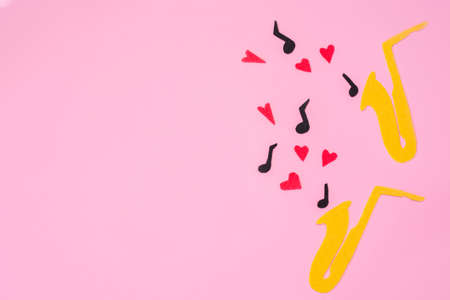 A cutted out of felt saxophones from which hearts and melodies flew out, on a pink background. Flat lay. International Jazz Day. Copy space.の写真素材