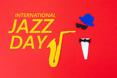 Silhouette of a musician with a saxophone from which melodies flew out, on a red background, cutted out of felt. Flat lay. Jazz day.の写真素材