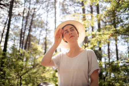 Portrait of a young woman in a straw hat, wiping sweat from her forehead. Summer. The concept of protection from sunstroke.の写真素材