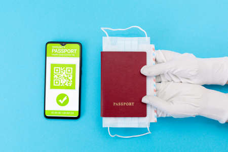 Hands in protective gloves give a passport with mask. Cellphone screen with an electronic health passport with qr-code. Flat lay. Concept of Covid-19 test for travel.の写真素材