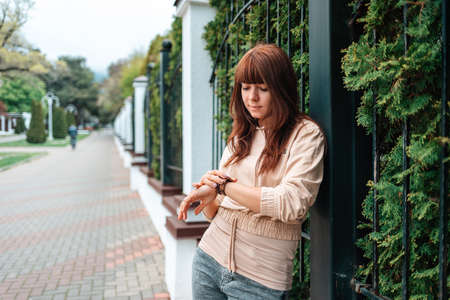 A young pretty woman looks at her wristwatch. Outdoor. The concept of waiting.の写真素材