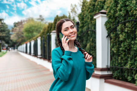 Portrait of a cute smiling woman with pigtails talking on the phone. In the background fence with trees.の写真素材