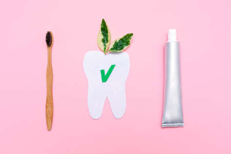 Eco and hygiene. A bamboo toothbrush, toothpaste and cut out tooth of felt with leafs. Flat lay. Pink background. Concept of eco-friendly hygiene objects.の写真素材